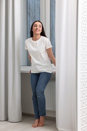 Photo of Young woman in stylish jeans near window indoors