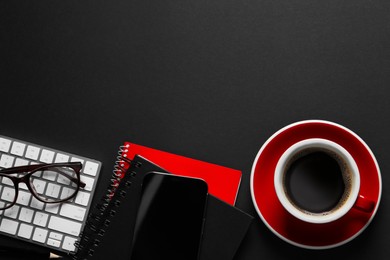 Photo of Cup with aromatic coffee, smartphone, notepads, glasses, pencil and keyboard on black background, flat lay. Space for text