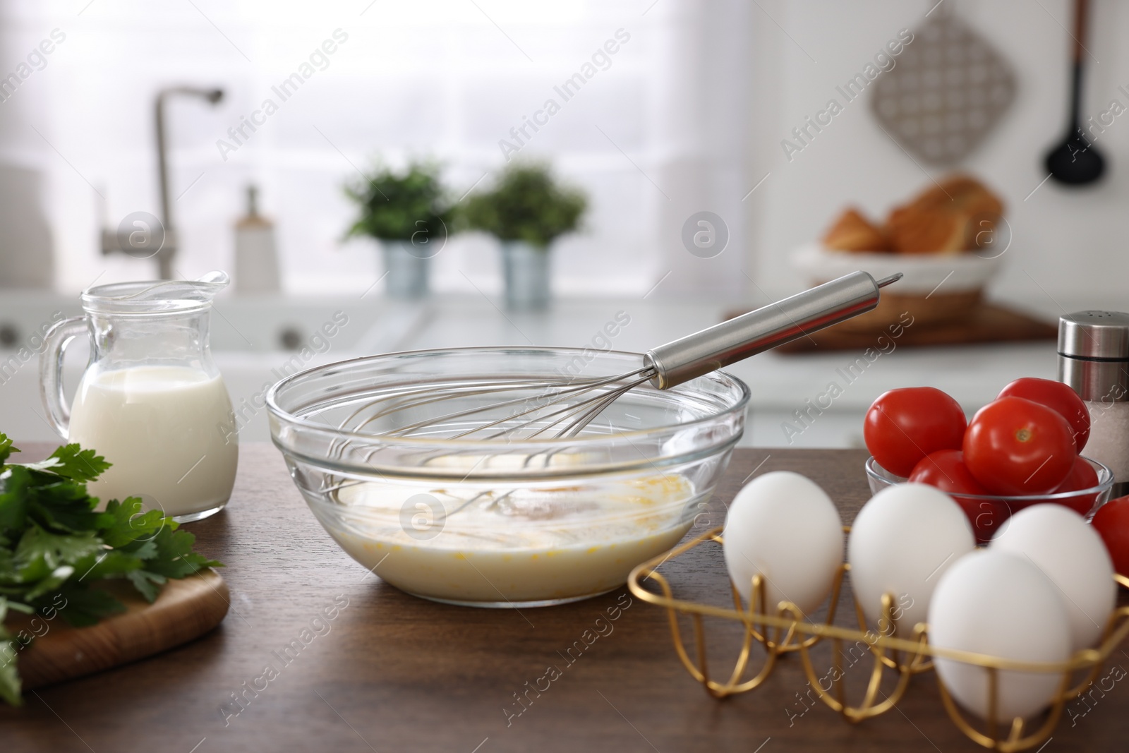 Photo of Whisk, bowl, beaten eggs and other ingredients on wooden table indoors