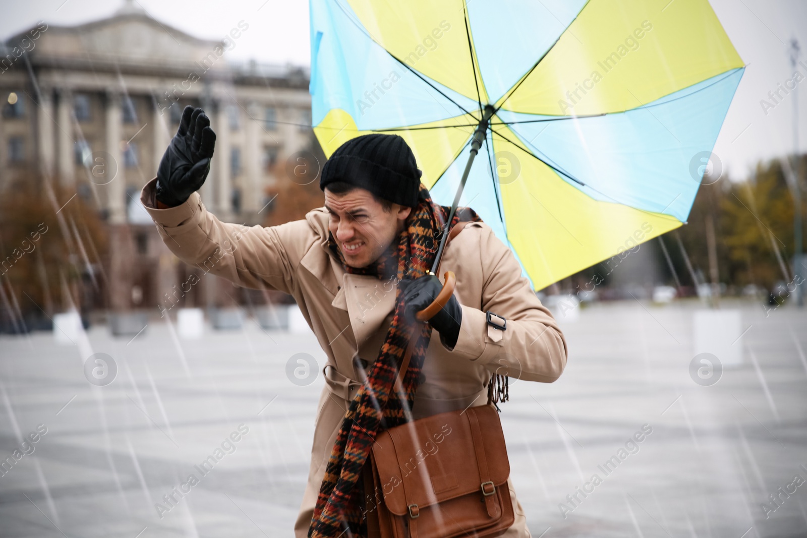 Photo of Man with colorful umbrella caught in gust of wind on street