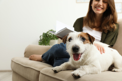 Photo of Young woman reading book and her cute Jack Russell Terrier on sofa at home. Lovely pet