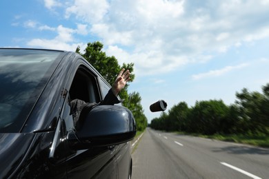 Photo of Driver throwing away paper coffee cup from car window. Garbage on road