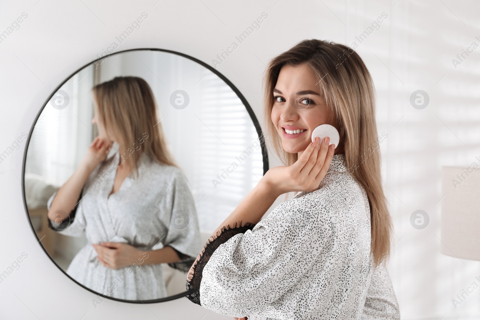 Photo of Beautiful young woman cleaning her face near mirror in room