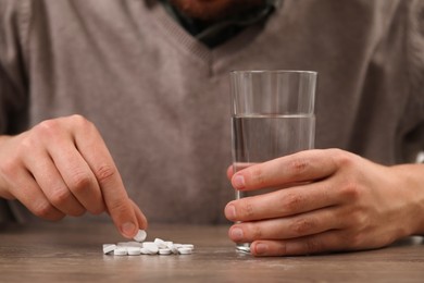 Photo of Man with glass of water and antidepressant pills at wooden table, closeup