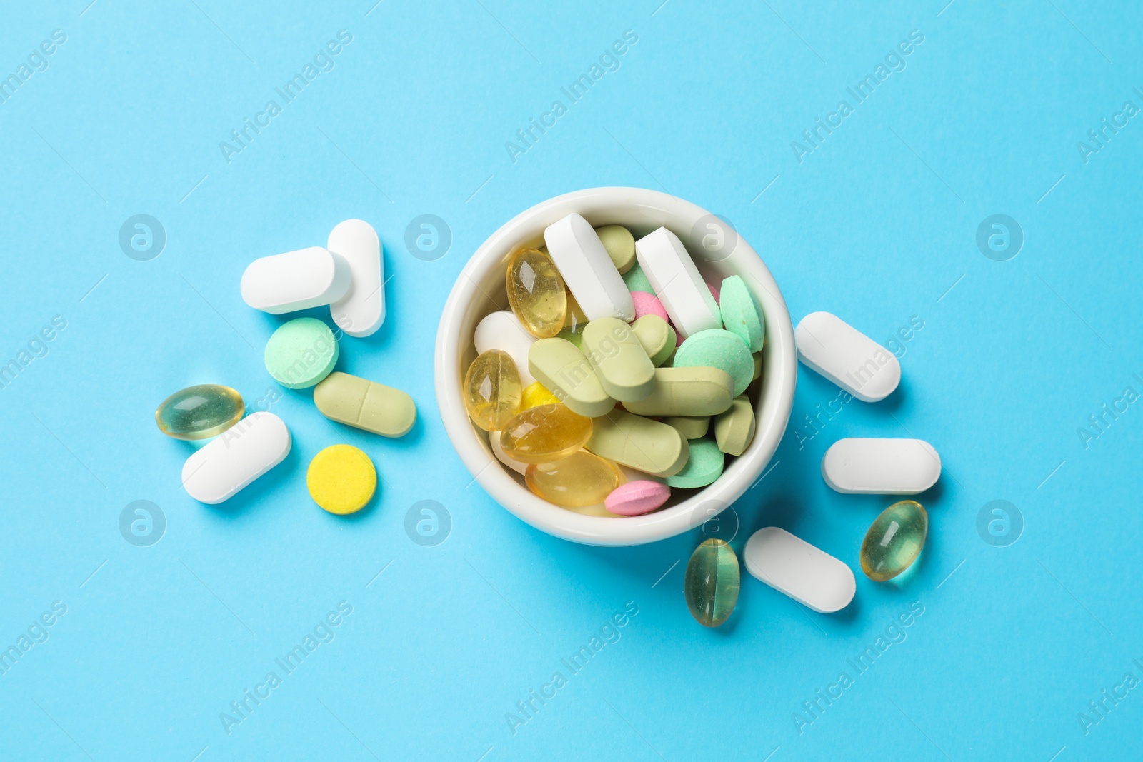 Photo of Different vitamin pills in bowl on light blue background, top view