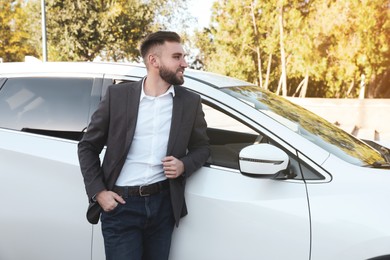 Handsome young driver near modern car on city street