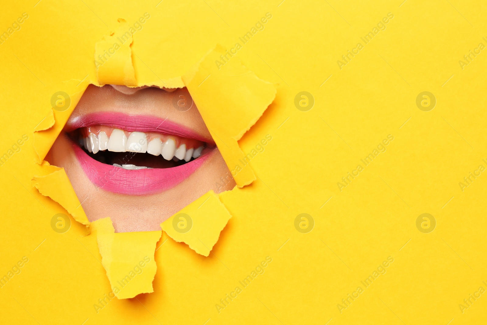 Photo of Lips of young woman with beautiful lipstick visible through hole in color paper. Space for text