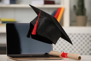 Graduation hat, student's diploma and laptop on white table indoors