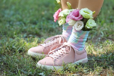 Photo of Woman standing on green grass with flowers in socks, closeup