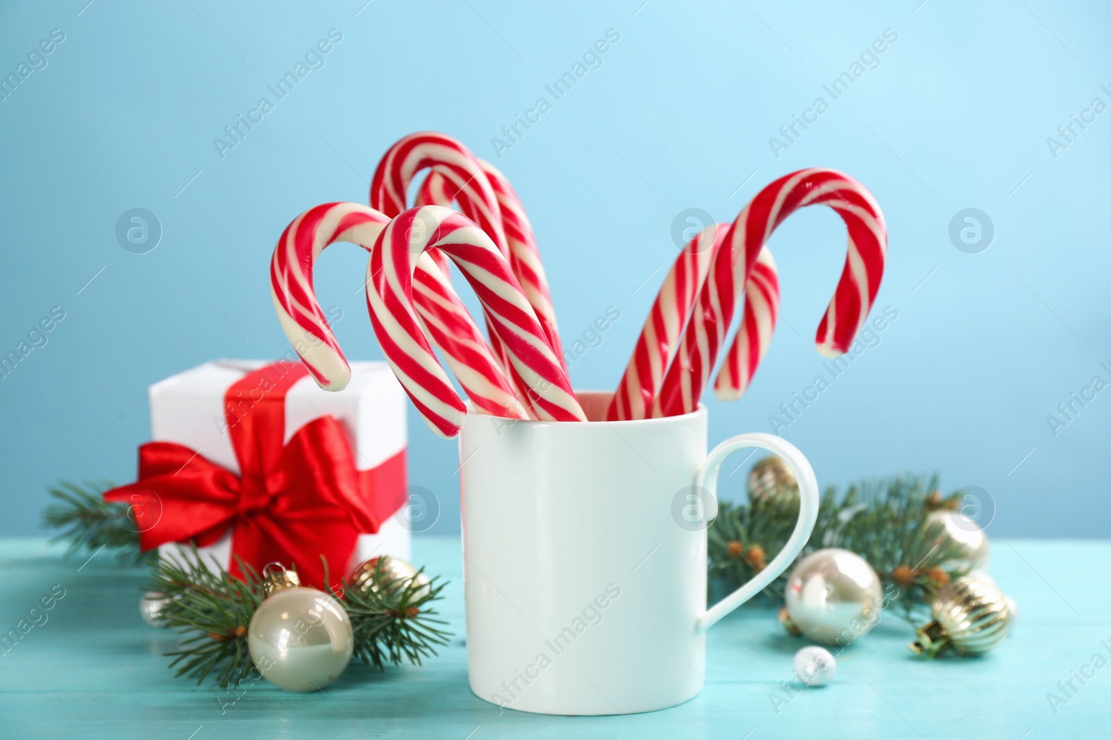 Photo of Many sweet candy canes in cup and Christmas decor on light blue wooden table
