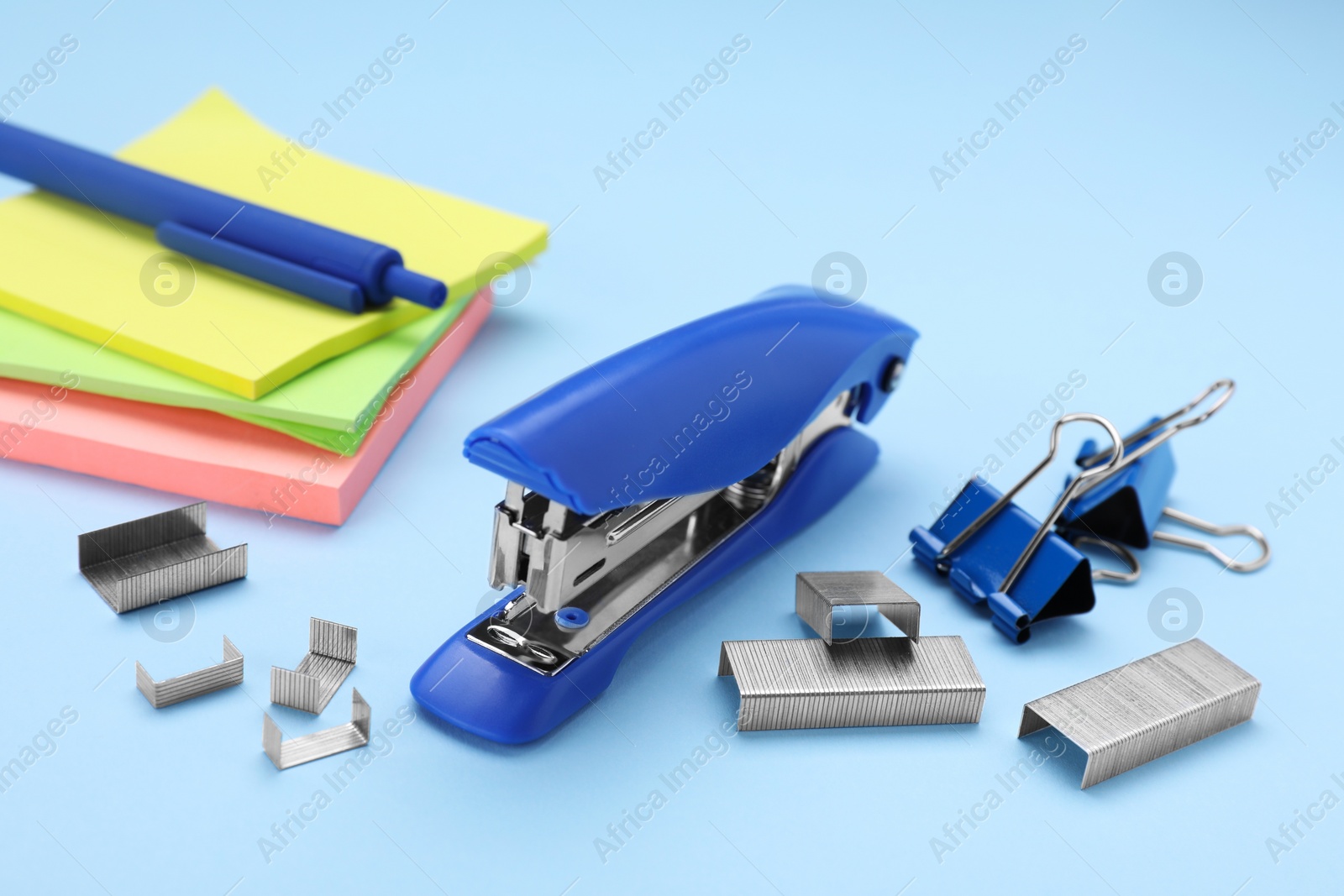 Photo of New bright stapler with stationery on light blue background