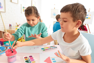 Photo of Cute little children painting their palms at table in room