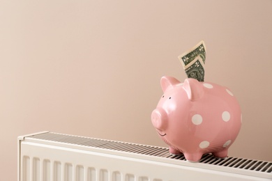 Heating radiator with piggy bank and money on color background