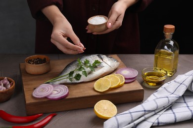 Photo of Woman salting raw dorado fish at grey table, closeup