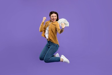 Photo of Excited woman with dollar banknotes jumping on purple background