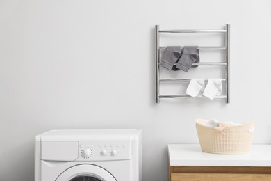 Photo of Heated towel rail with socks on white wall in bathroom, space for text
