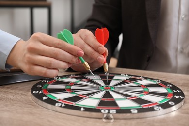 Photo of Business targeting concept. Man and woman with darts aiming at dartboard at wooden table indoors, closeup