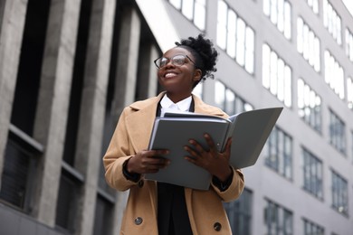 Happy woman with folders outdoors, low angle view. Lawyer, businesswoman, accountant or manager