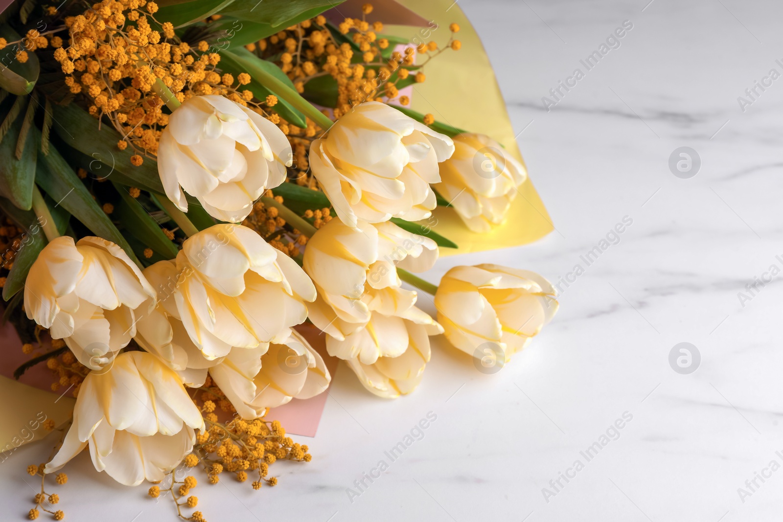 Photo of Bouquet with beautiful tulips and mimosa flowers on white marble table. Space for text