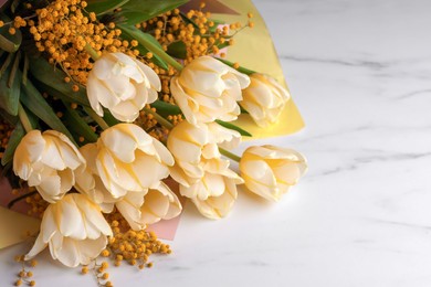 Bouquet with beautiful tulips and mimosa flowers on white marble table. Space for text