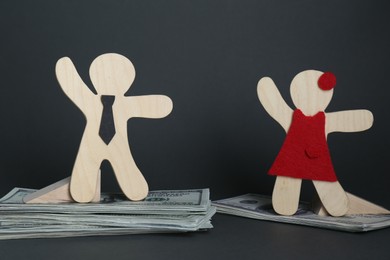 Photo of Gender pay gap. Wooden figures of man and woman on dollar banknotes against black background