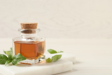 Photo of Bottle of essential basil oil and fresh leaves on white wooden table, space for text