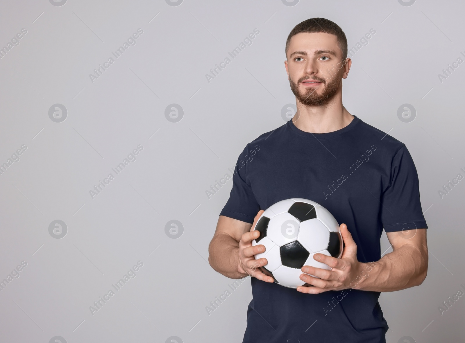 Photo of Athletic young man with soccer ball on light grey background. Space for text