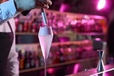 Photo of Bartender adding foam onto alcoholic cocktail at counter in bar, closeup. Space for text