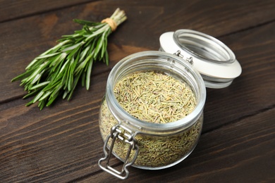 Photo of Jar of dried rosemary and fresh branches on wooden table