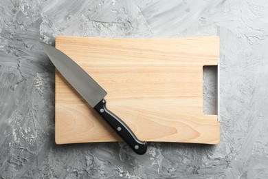 Photo of Knife and wooden board on grey textured table, top view