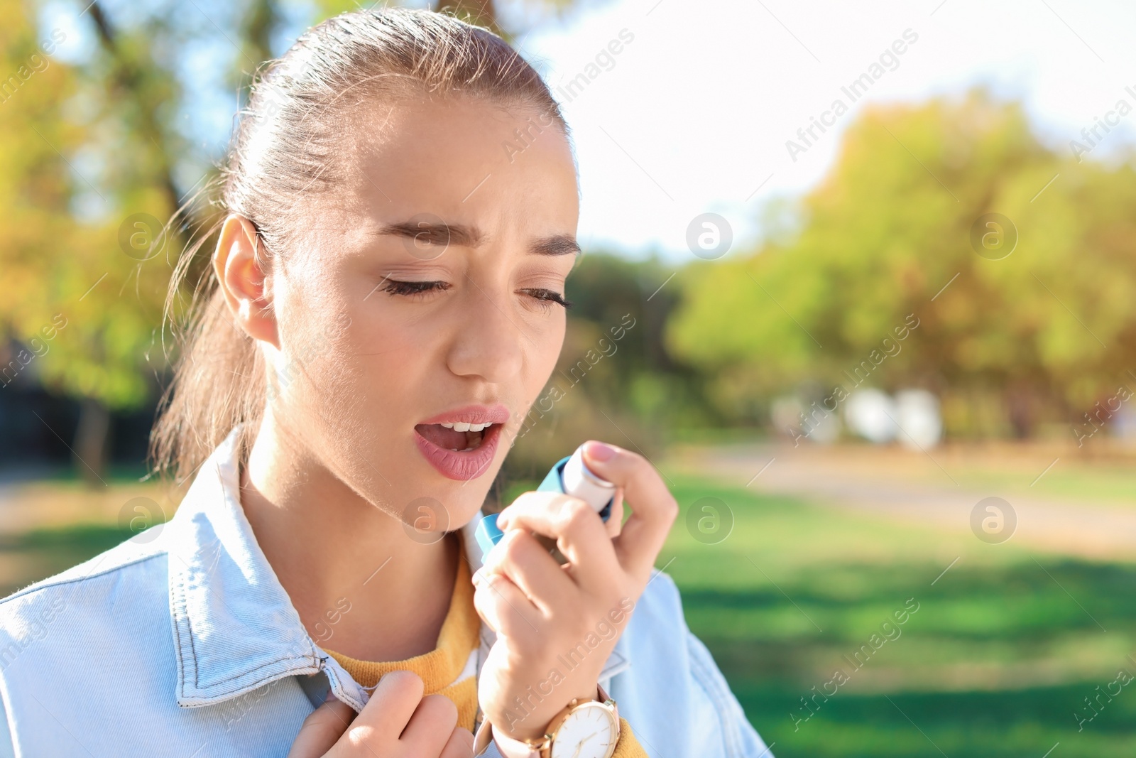 Photo of Young woman using asthma inhaler outdoors. Space for text