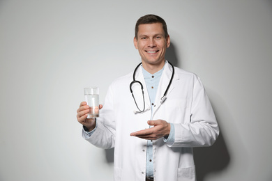 Photo of Nutritionist holding glass of pure water on light grey background