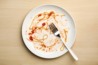 Photo of Dirty plate with food leftovers and fork on wooden background, top view