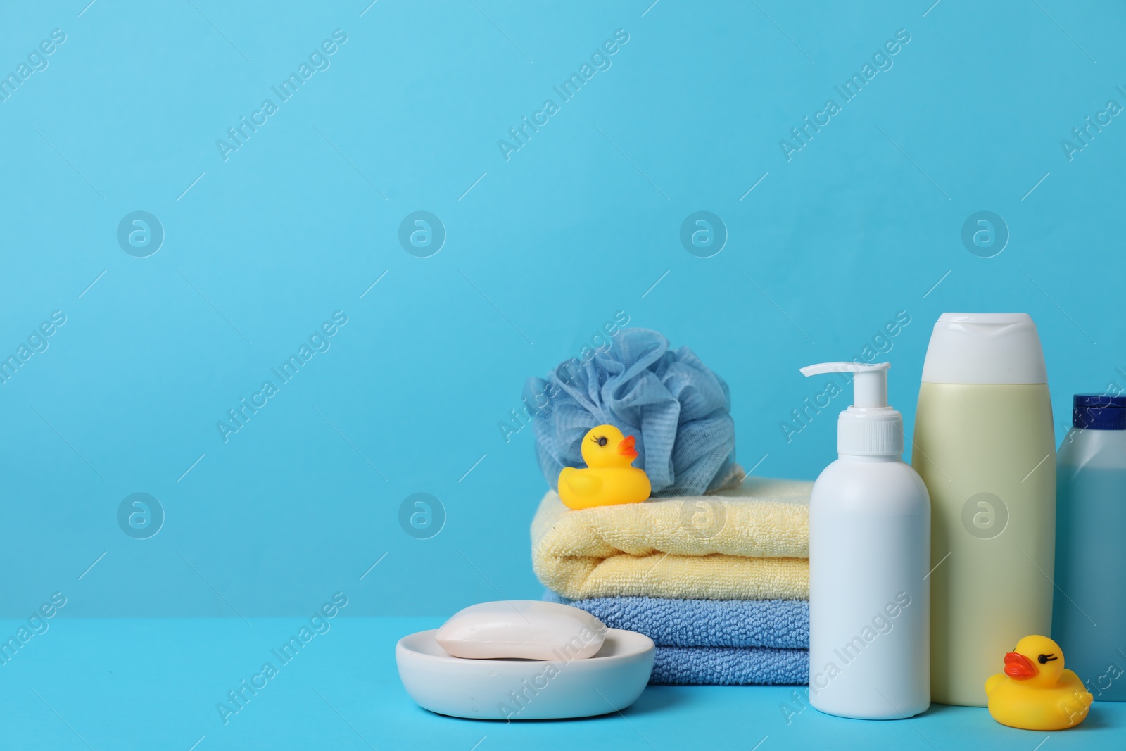 Photo of Baby cosmetic products, bath ducks, sponge and towels on light blue background. Space for text