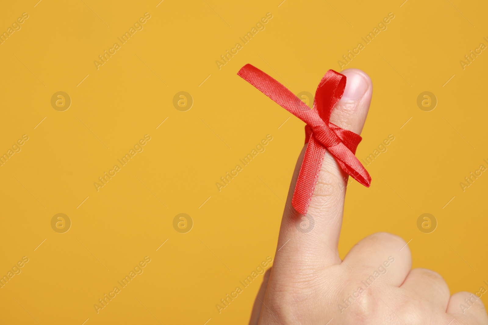 Photo of Man showing index finger with red tied bow as reminder on orange background, closeup. Space for text