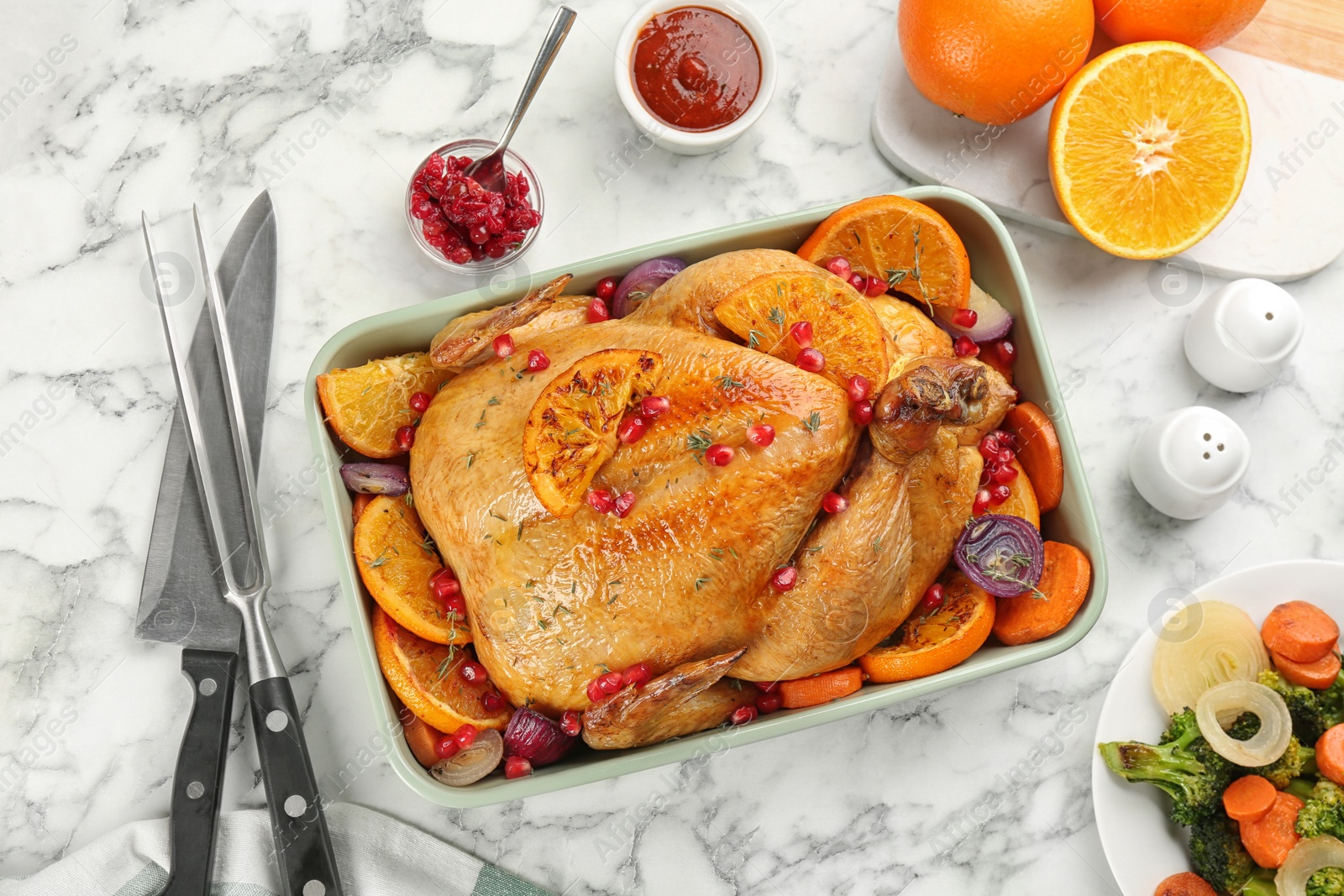 Photo of Roasted chicken with oranges, pomegranate and vegetables on white marble table, flat lay