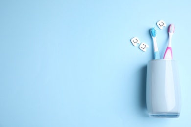 Toothbrushes in holder on light blue background, flat lay. Space for text