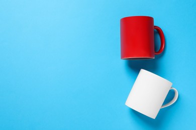 Photo of White and red ceramic mugs on light blue background, flat lay. Space for text