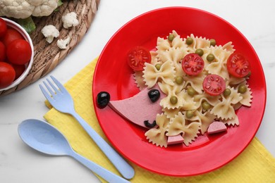 Photo of Plate with cute hedgehog made of delicious pasta, sausages and tomatoes on white table, flat lay. Creative serving for kids