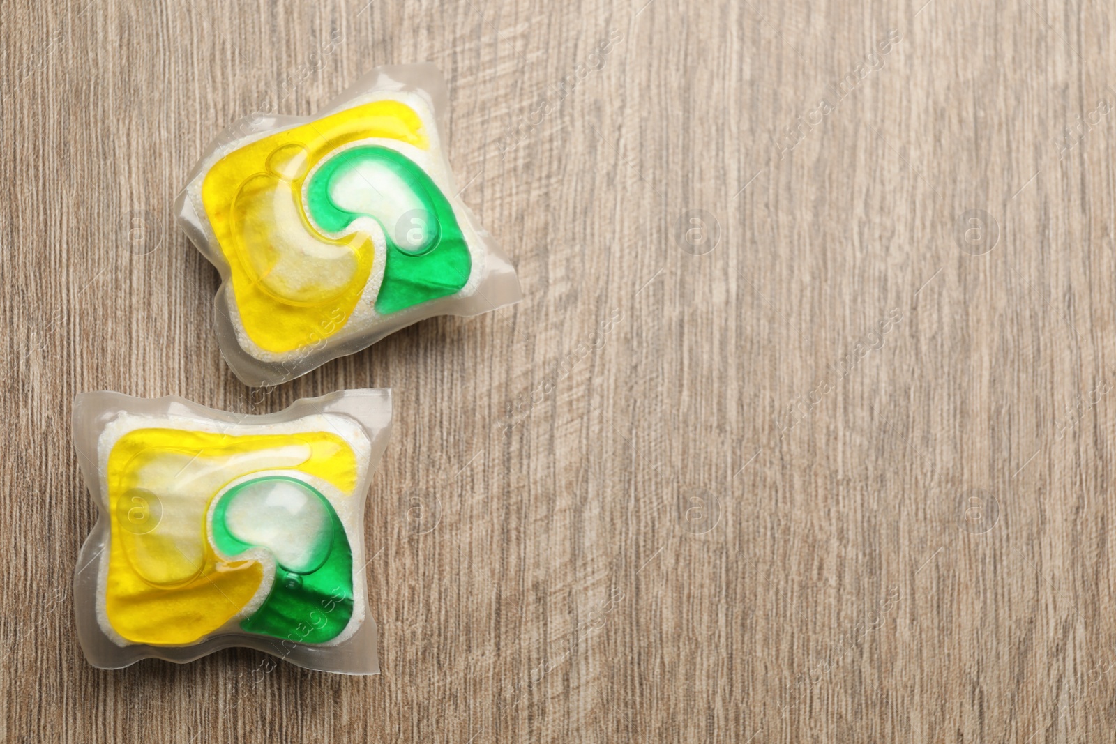 Photo of Two dishwasher detergent pods on wooden table, flat lay. Space for text