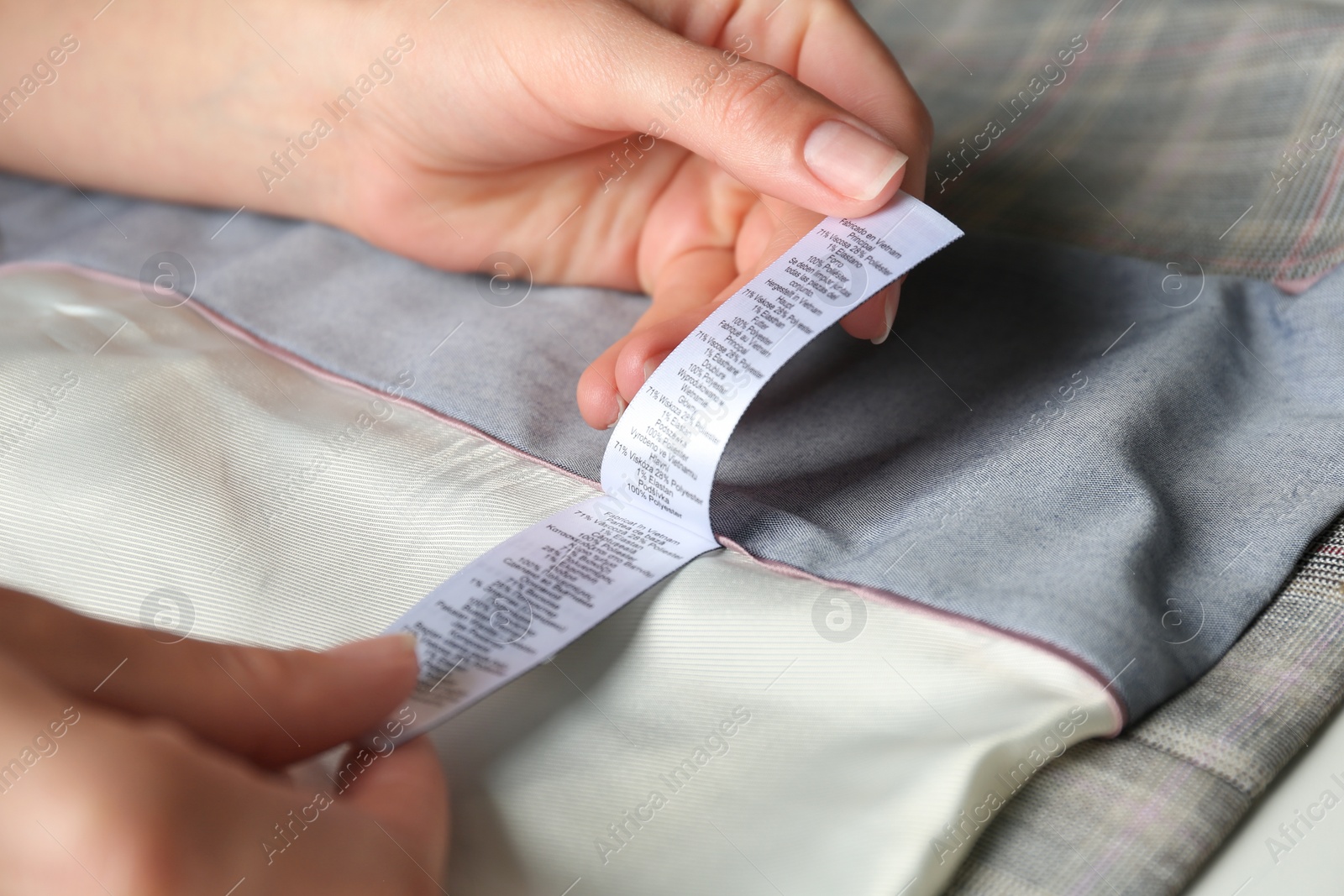 Photo of Woman reading clothing label with content information on light garment, closeup