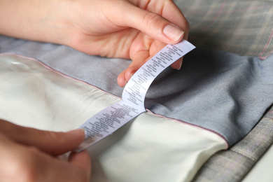 Photo of Woman reading clothing label with content information on light garment, closeup