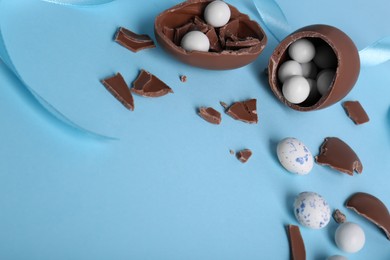 Photo of Tasty broken chocolate eggs with different sweets on light blue background. Space for text