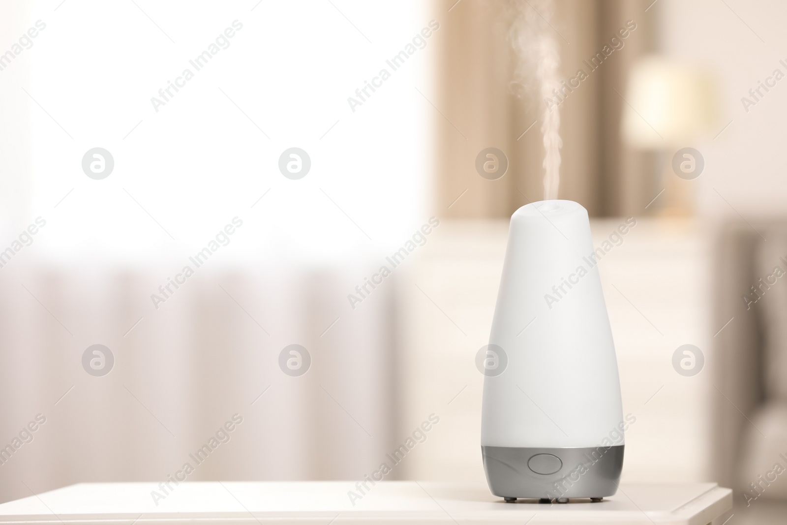 Photo of Modern essential oil diffuser on table indoors. Space for text