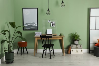 Photo of Typewriter, stack of papers and mood board on wooden table near pale green wall. Writer's workplace