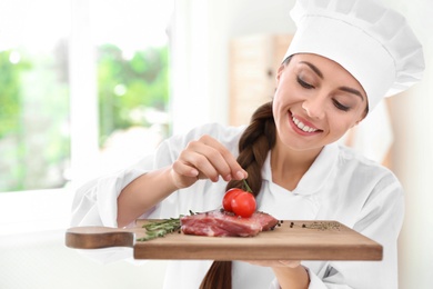 Photo of Professional female chef holding board with meat in kitchen