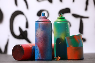 Many spray paint cans and caps on gray surface against white wall with different drawn symbols