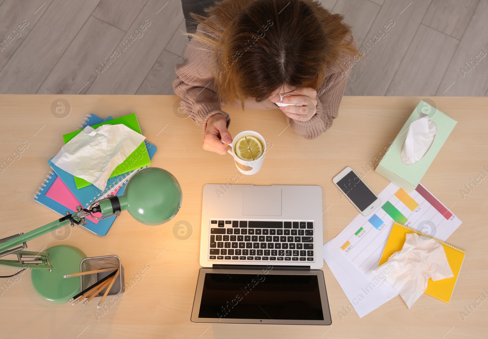 Photo of Exhausted woman with tissue and cup of hot drink suffering from cold while working with laptop at table, top view