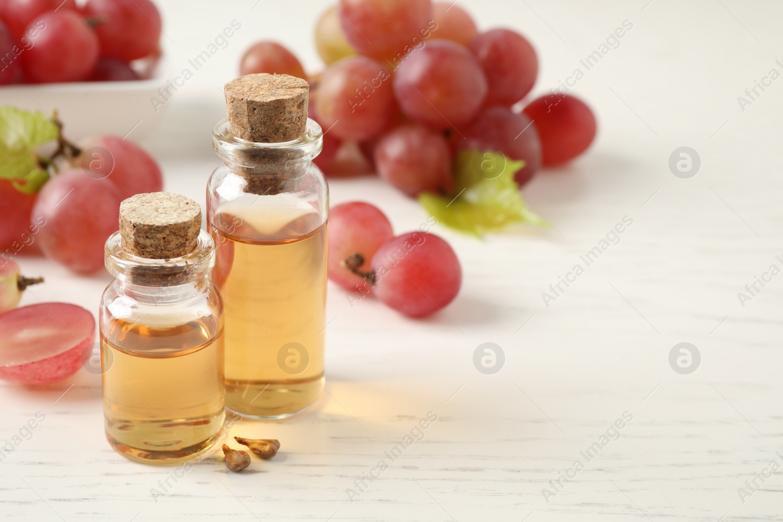 Photo of Organic red grapes, seeds and bottles of natural essential oil on white wooden table