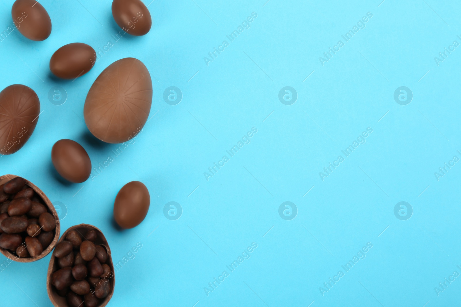 Photo of Sweet chocolate eggs on light blue background, flat lay. Space for text